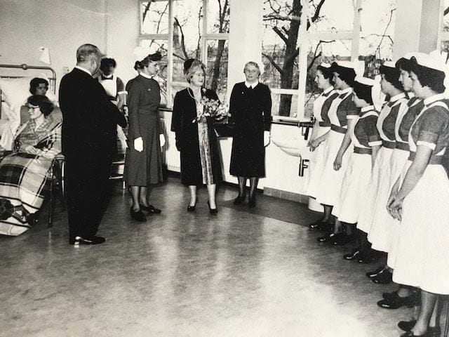 Black & white photo of the Queen Mother meeting a line-up of nurses in a ward.